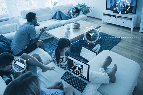 A family seating on two couches, watching tv, looking at their laptop screens, phones and other electronic devices